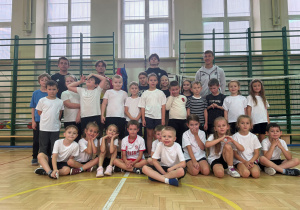 Uczniowie, trener i zawodnicy Łódzkiego Klubu Sportowego na wspólnym zdjęciu po treningu. Zdjęcie wykonane na sali gimnatycznej na tle drabinek