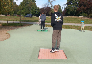 Uczniowie klasy VIII w pobliskim parku na placu zabaw wykonują doświadczenia poznając zjawisko ruchu drgającego - uczeniowie skaczą na trampolinie