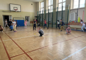 Przedszkolaki na sali gimnastycznej bawią się w ,,kucanego berka".