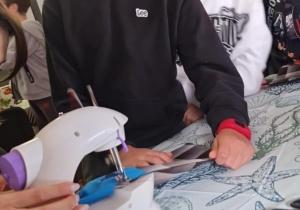 Uczniowie klasy IV uczą się szyć. Pani prowadząca pokazuje jak korzystać z maszyny do szycia.