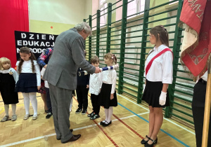 Pan Dyrektor mianuje uczniów dotykając ramienia ucznia dużym piórem