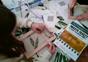 Uczennica z klasy VI na prostym narzędziu tkackim próbuje tkać z wełny