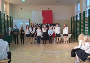 Uczniowie ustawieni w rzędzie na tle polskiej flagi i dekoracji z okazji Święta Niepodległości, którzy brali udział w przedstawieniu