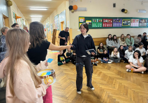 Uśmiechnięta uczennica odbiera karteczkę z życzeniami, wręczają kartkę dziewczyny z Samorządu Uczniowskiego