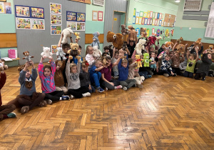 Spotkanie klas I-III na korytarzu. Każde dziecko trzyma w górze swoją ulubioną maskotkę.