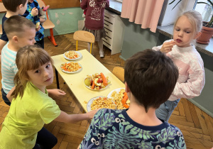 Poczęstunek dla uczniów naszej szkoły. Na stoliku leżą pokrojone na talerzach jabłka i marchewki, uczniowie się częstują.