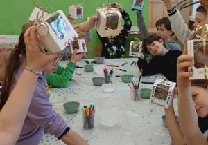 Uczniowie unoszą do góry swoje ozdobione pudełeczka z własnoręcznie wykonaną bombką czekoladową.
