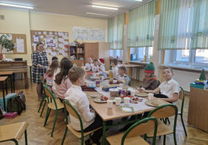 Klasa czwarta wraz z wychowawcą siedzi przy stołach podczas swojej wigilii