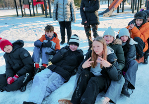Uczniowie klasy VI pozują na śniegu w tle jest plac zabaw i drzewa parku.