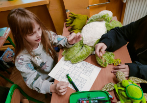 Uczennica siedzi przy szkolnej ławce, intensywnie analizując arkusz z sudoku.