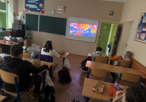 Uczniowie oglądają film na tablicy multimedialnej i zajadają się popcornem