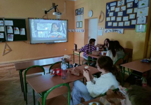 Uczniowie oglądają film na tablicy multimedialnej i zajadają się popcornem