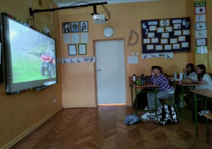 Uczniowie oglądają film na tablicy multimedialnej i zajadają się popcornem