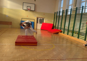 Trener Judo pokazuje rzut na jednym z dzieci uczestniczących w treningu na sali gimnastycznej