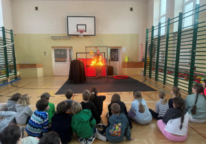 Dzieci siedzą i z zaciekawieniem obserwują przedstawienie, a Pan Bańka robi pokazy z ogniowych baniek