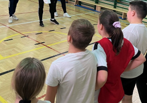 sala gimnastyczna, uczestnicy stoją i słuchają zasad gry.
