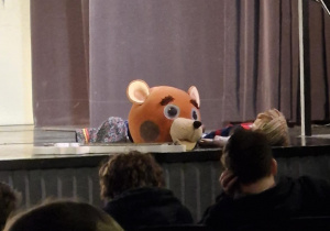 Scena teatru a na niej jeden z uczestników półkolonii leży na scenie a obok niego duży pluszowy miś.