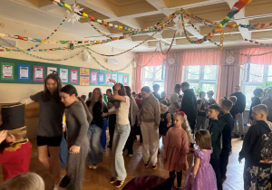 Uczniowie na korytarzu szkolnym podczas zabawy karnawałowej w rytm znanej i kochanej ,,Belgijki" tańczą w parach.