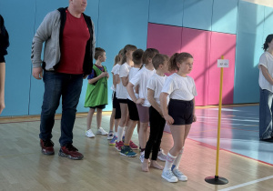 Zawodnicy z naszej szkoły ustawieni ,,gęsiego" przygotowani do startu. Obok nich stoi pan Remek i motywuje ich do rywalizacji. Wyżej jest balkon na którym stoją dzieci i dorośli dopingując swoich kolegów.