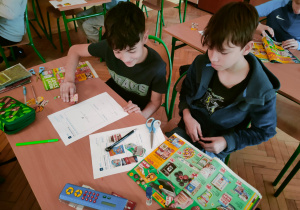 Uczniowie klasy 5 analizują gazetki reklamowe, wycinając i naklejając produkty na karty pracy.