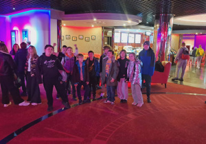 Uczniowie naszej szkoły pozują do zdjęcia przed wejściem na salę kinową, wszyscy w dobrych nastrojach.