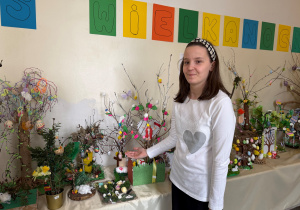 Uczennica klasy V podczas odbioru nagród, pozuje na tle napisu Wielkanoc prezentując swoją pracę