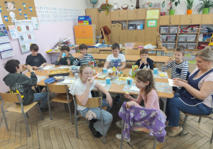 Uczniowie klasy 2 siedzą przy stole i zajadają się smakołykami przygotowanymi przez rodziców.