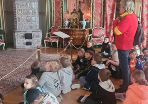 Uczniowie klasy I i II w Pałacu w Bolimowie, siedzą na podłodze w sali pałacowej wokoło dzieci kolorowe firany i zdobienia na ścianach. Uczniowie słuchają przewodnika.