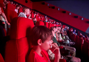 Sala kinowa w kinie Cinema City, uczniowie siedzą w fotelach oglądając film i zajadając się popcornem.