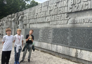 Uczniowie klasy czwartej pod pomnikiem Rewolucjonistów w Parku im. Józefa Piłsudskiego. Trzech uczniów stoi trzymając znicz.