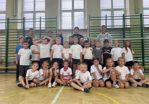 Uczniowie, trener i zawodnicy Łódzkiego Klubu Sportowego na wspólnym zdjęciu po treningu. Zdjęcie wykonane na sali gimnatycznej na tle drabinek