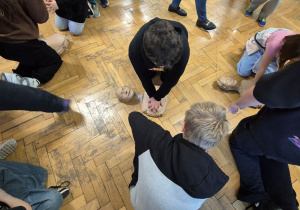 Uczniowie szkoły zgromadzeni na korytarzu, chłopiec wykonuje RKO.